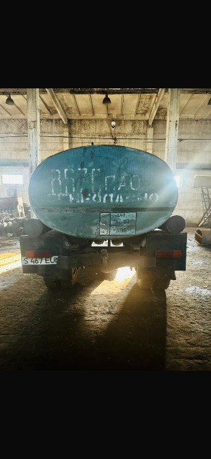 Вид сзади старого грузовика с неразборчивой надписью на баке, окружённого индустриальной атмосферой