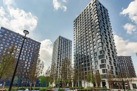 Современные высотные здания с панорамными окнами и зелеными насаждениями на фоне голубого неба и облаков