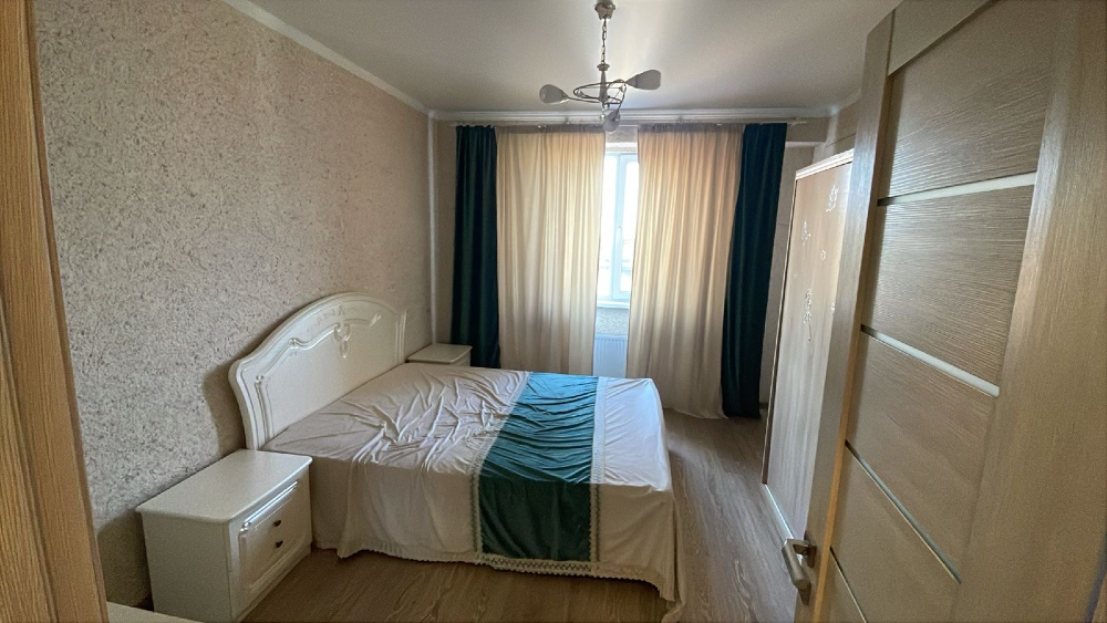 Есіктен көрініс, екі адамдық төсектері мен жеңіл перделері бар жатын бөлме