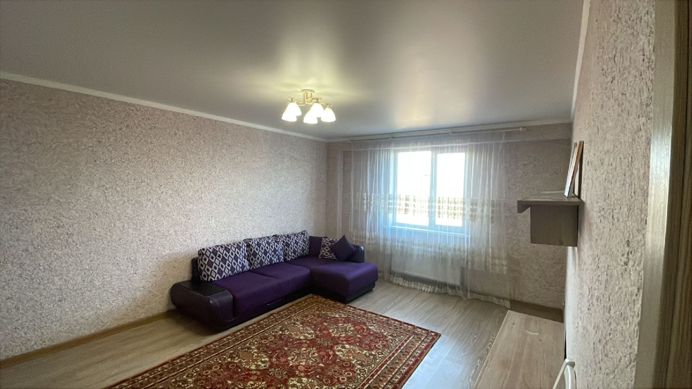 Күлгін диван мен едендегі кілемімен безендірілген терезелері перделермен жабылған бөлме