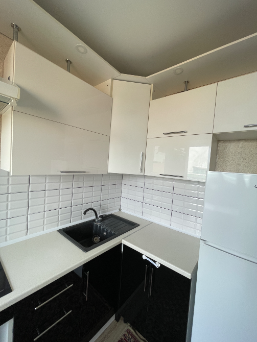 Ақ және қара шкафтар, жуу құралы мен плита орналасқан асхана