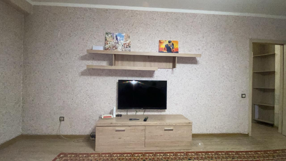 Телевизор мен қабырғада суреттермен безендірілген сөресі бар қонақ бөлме