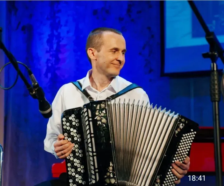 Игрок на баяне во время выступления на сцене с синей подсветкой