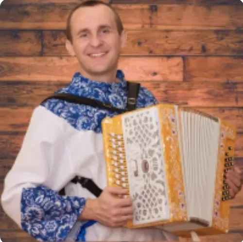 Игрок на баяне в традиционном русском костюме на фоне деревянной стены