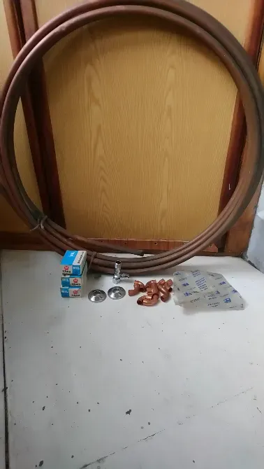 Медные трубы в катушке, фитинги, сантехнические элементы и упаковка с аксессуарами на фоне стены