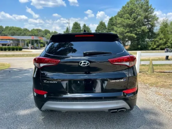 Задняя часть черного Hyundai Tucson с видимыми задними фонарями и надписью 