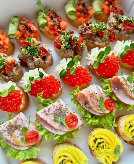 Разнообразные канапе с красной икрой, мясом и овощами на белом фоне