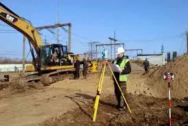 Құрылыс учаскесінде экскаватордың фонында геодезиялық жұмыстар жүргізетін маман