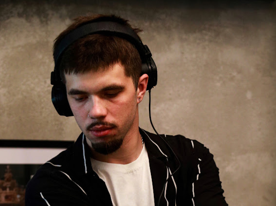 Жас жігіт құлаққапта, музыканы немесе диджейингті шоғырланумен айналысып, текстуралы қабырға фонында.