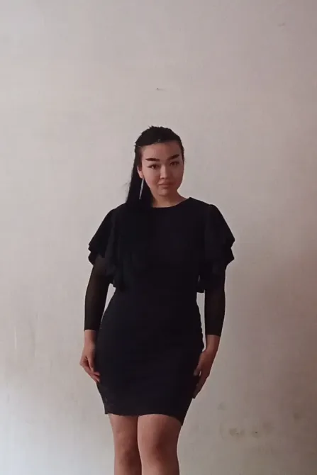 Женщина в черном платье на фоне светлой стены