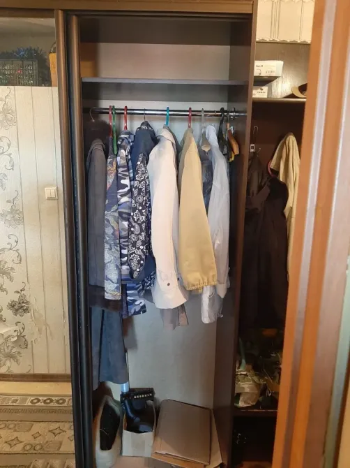 Әр түрлі киімдер ілулі тұрған ілгіштері бар шкаф