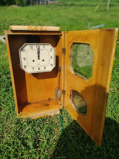 Деревянные настенные часы с круглым циферблатом на фоне зелёной травы