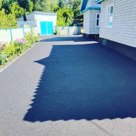 Новое асфальтное покрытие во дворе частного дома с цветами и забором