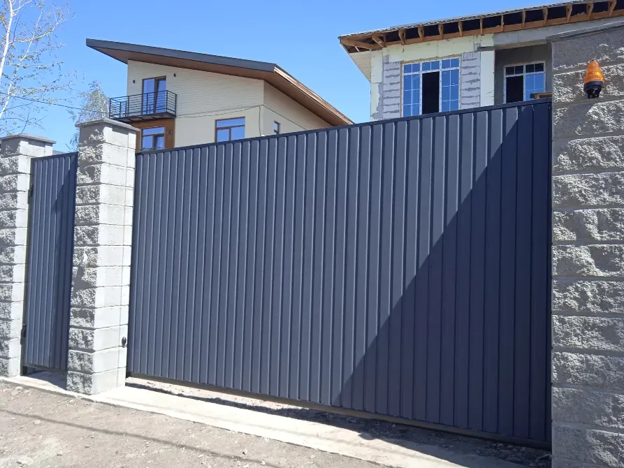 Тік планкалармен жасалған сұр материалдан жасалған есік, фондағы үймен