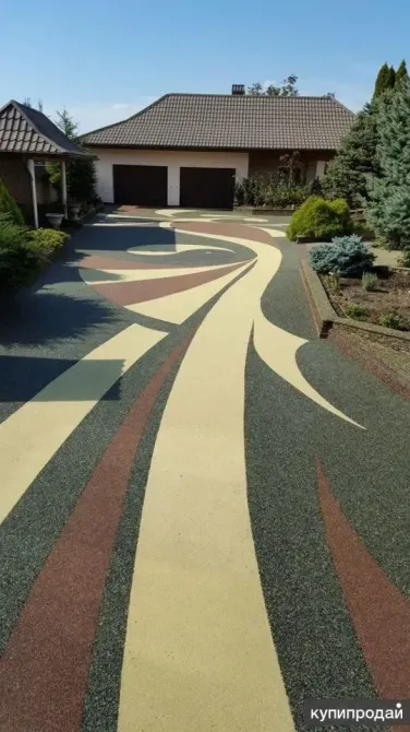 Дорога с декоративным покрытием, оформленная в ярких цветах, ведет к дому с двухскатной крышей