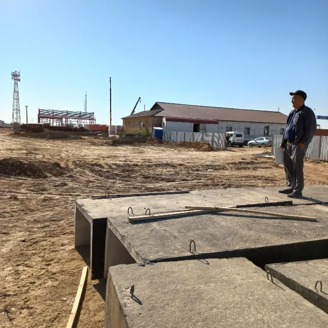 Мужчина стоит на строительной площадке, смотрит вдаль на земляные работы и строящиеся здания