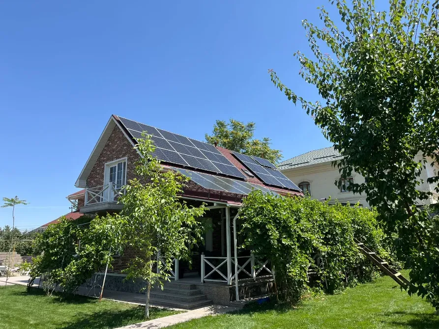 Крышадағы күн панельдерімен қоршалған үй, ағаштармен оралған