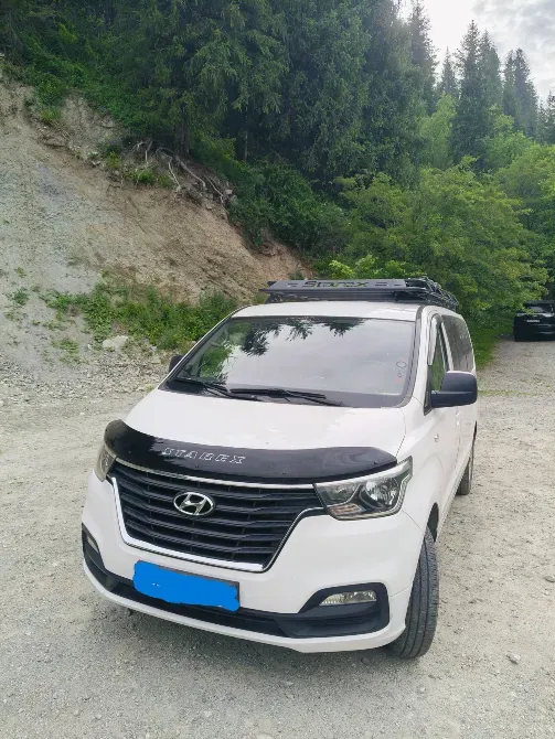 Ақ Hyundai минивэні ағаштары бар табиғи көріністің фонында