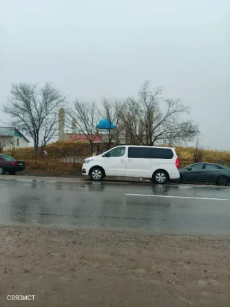 Белый минивэн на мокрой дороге с деревьями на заднем плане