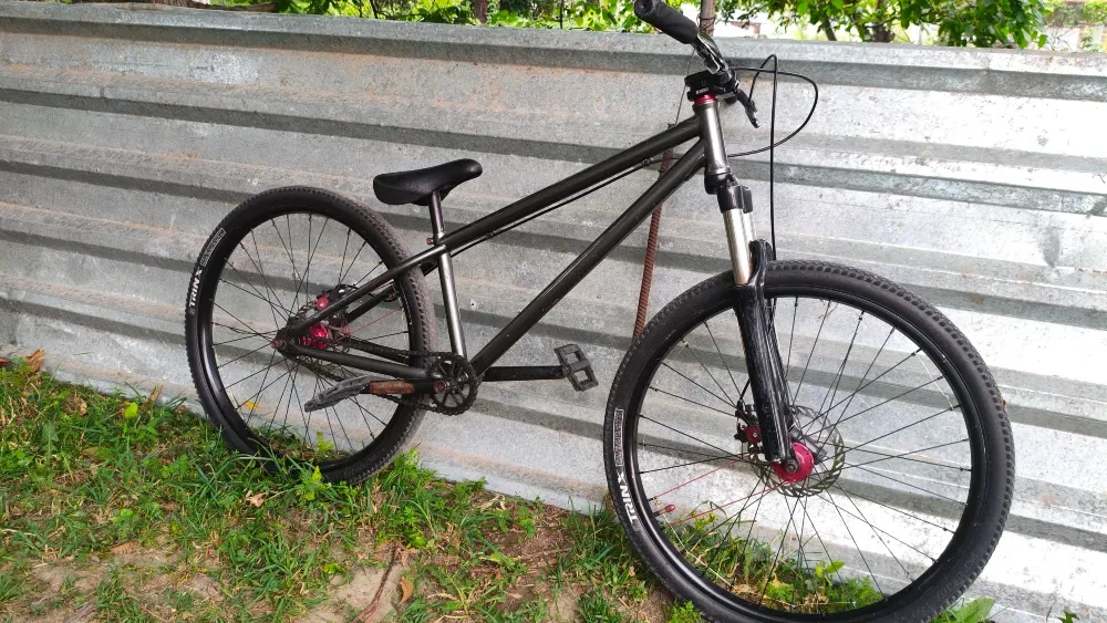 Қара түсті велосипед металл қабырғаның жанында орналасқан, шиналары бар