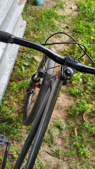 Трава мен металл конструкциясының фонында қара жақтаулы велосипедтің тұтқасы және алдыңғы бөлігі