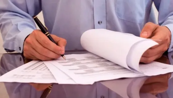 Мужчина заполняет бумаги и подписывает документы на столе