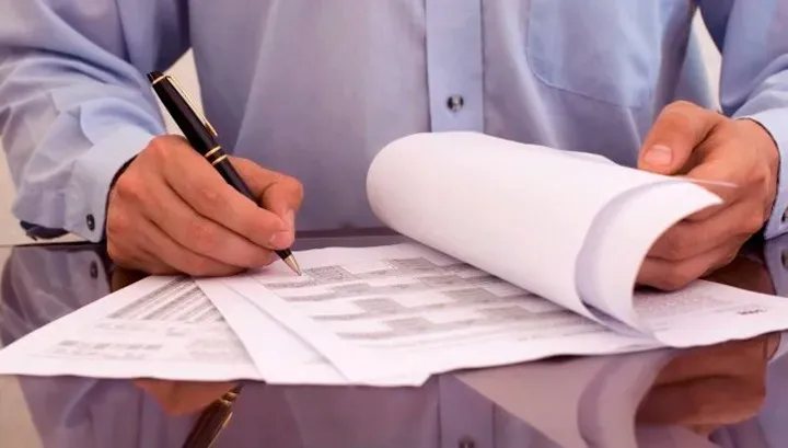 Мужчина заполняет бумаги и подписывает документы на столе