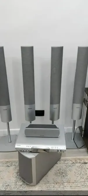 Аудиосистема с колонками и проигрывателем на фоне светлой стены. Колонки установлены вертикально, центральный динамик находится на столе