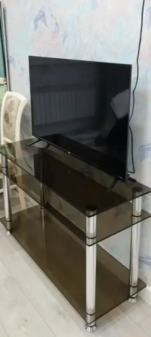 Әйнекті ТВ тумбасы, үстінде теледидар мен жанында орындық орналасқан.