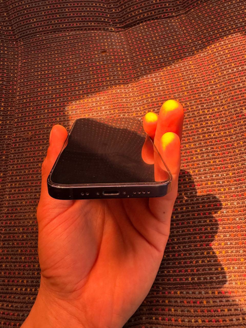 Смартфонның үстінен көрінісі, қара экранмен, қолда.