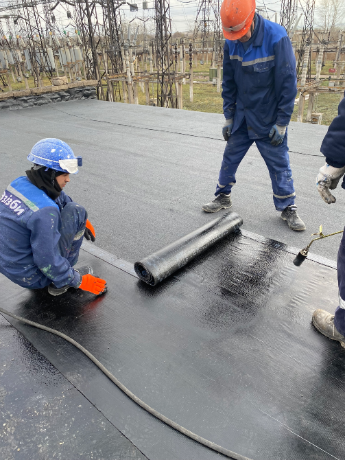 Шатырда рулонды материалды орнатушы жұмысшылар, олардың біреуі тізерлеп отыр