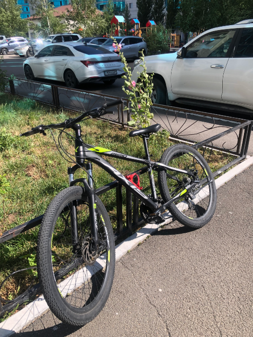 қара түсті велосипед, сары-жасыл элементтерімен автомобильдердің жанына тротуарда