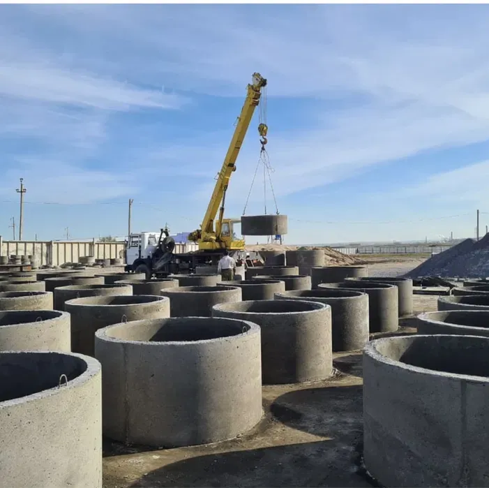 Строительная площадка с краном, поднимающим бетонный элемент над круглыми бетонными основаниями