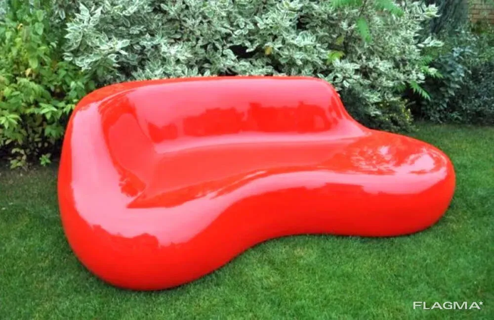 Яркая красная мягкая скамейка необычной формы на фоне зелени