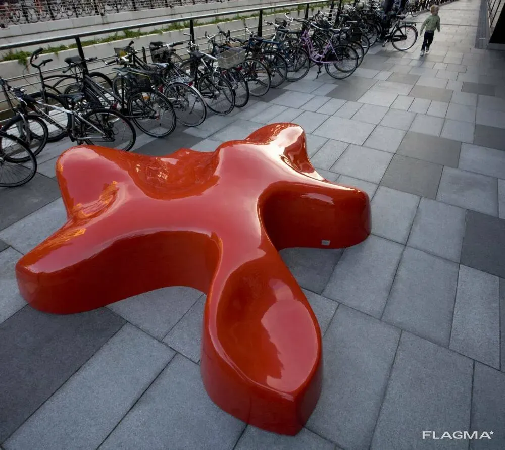 Красный необычный элемент мебели, напоминающий цветок, на тротуаре среди велосипедов