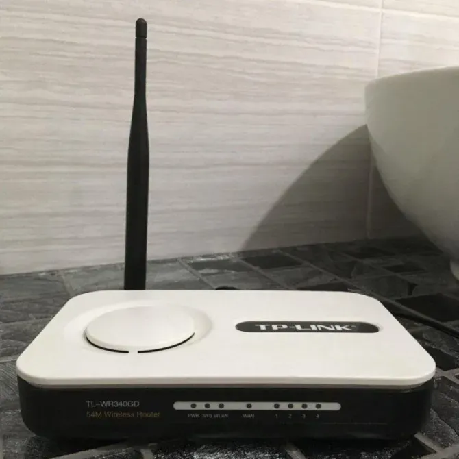 Беспроводной роутер TP-Link TL-WR340G с антенном на фоне плитки и раковины
