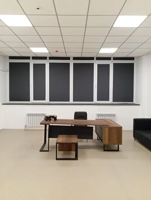 Офис с большими окнами и темными жалюзи, столом и стульем на переднем плане