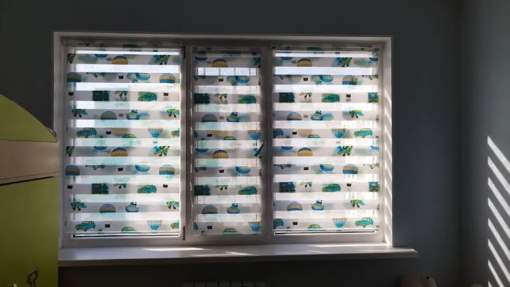 Окно с жалюзи в светлой комнате, на которых изображены солнечные пляжи и природа