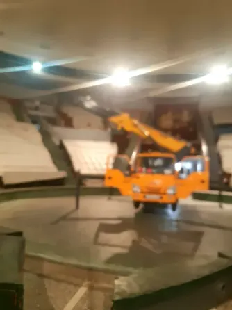 Грузовик с подъемником внутри помещения, где находятся белые конструкции