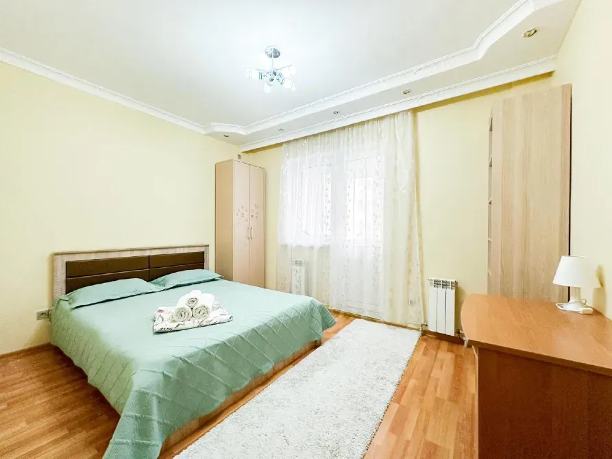 Спальня с зеленым покрывалом, светлыми стенами и деревянной мебелью