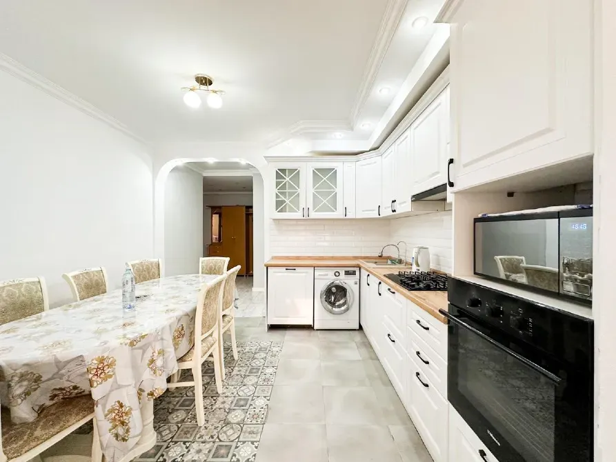 Кухня с большим обеденным столом, современной бытовой техникой и светлой отделкой