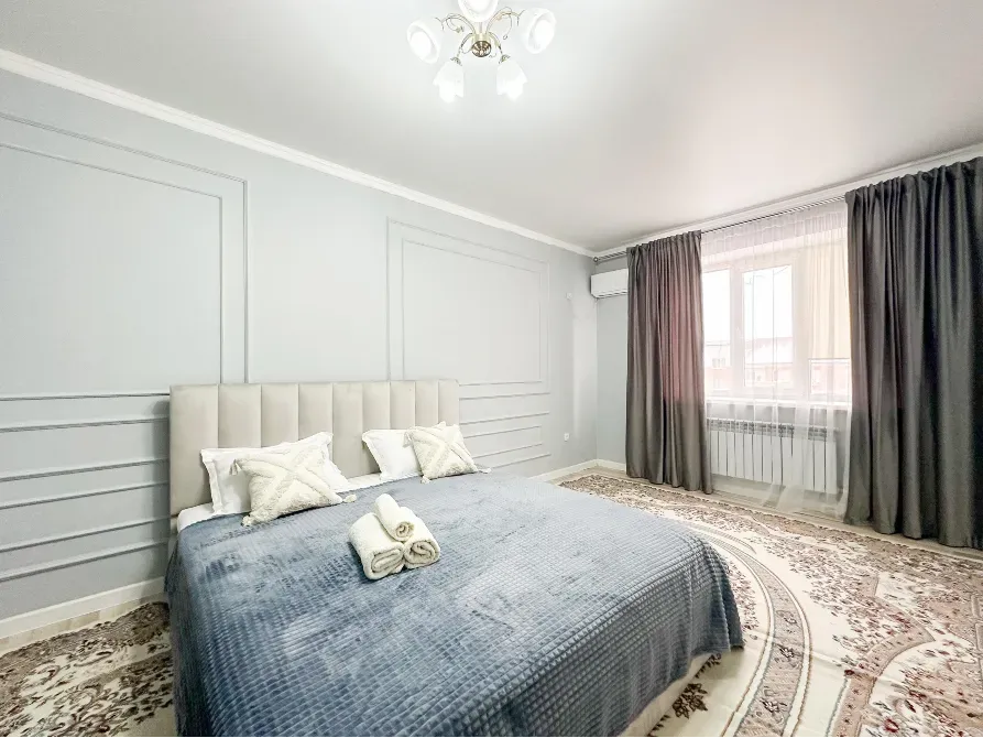 Спальня с коричневым покрывалом, большими окнами и серыми стенами