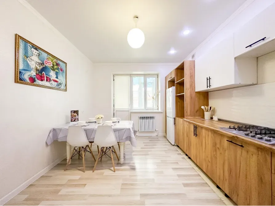 Кухня с обеденной зоной и деревянными шкафами, яркое освещение