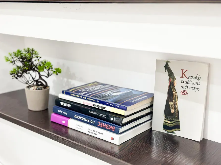 Книга о казахских традициях на полке с растением