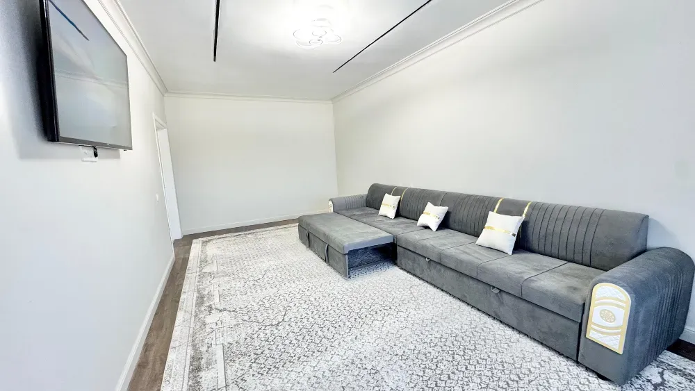 Кеъ кең қонақ бөлмесі сұр диванмен және қабырғада теледидармен