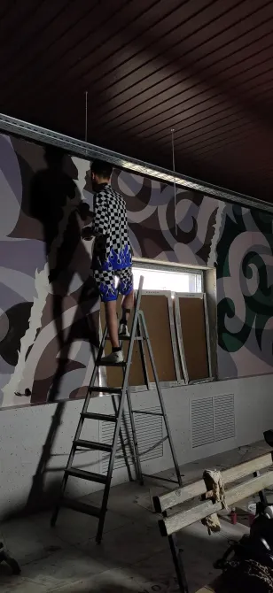 Художник рисует на стене с помощью лестницы