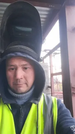 Рабочий в защитной одежде и шлеме для сварки, позируя на строительной площадке