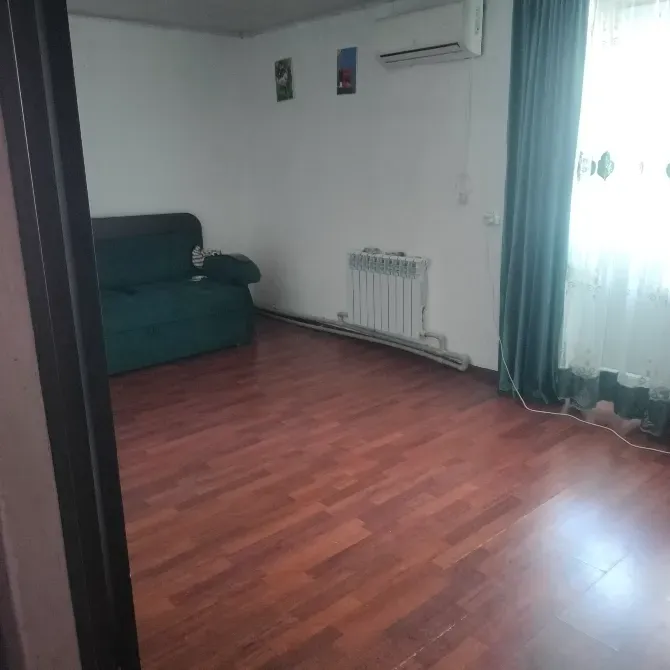 Пустая комната с диваном и паркетным полом, окна с шторками, квартира