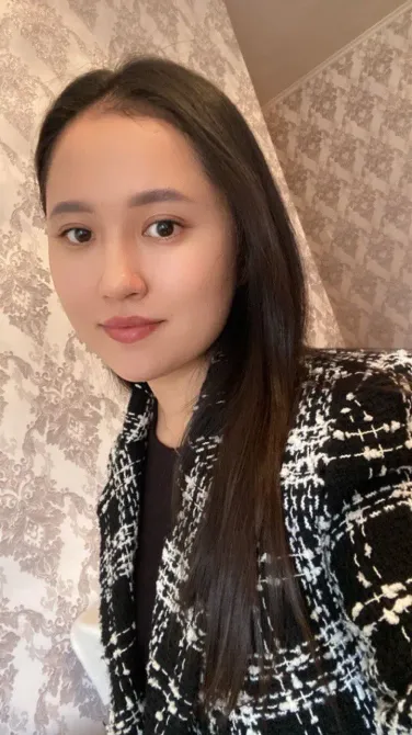 Женщина с длинными волосами в черно-белом жакете на фоне обоев в светлых тонах