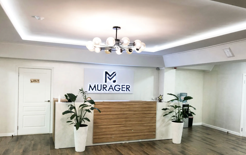 Murager логотипы барымен заманауи офис ресепшены, ағаш стенд және кәстрөлдердегі жасыл өсімдіктер.